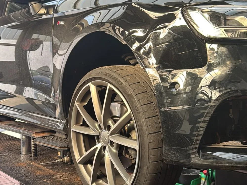 Schwarzer Audi auf der Hebebühne mit eingedrücktem Kotflügel vorne rechts
